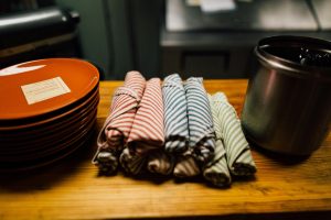 A cozy restaurant table setup with striped napkins, plates, and silverware container.